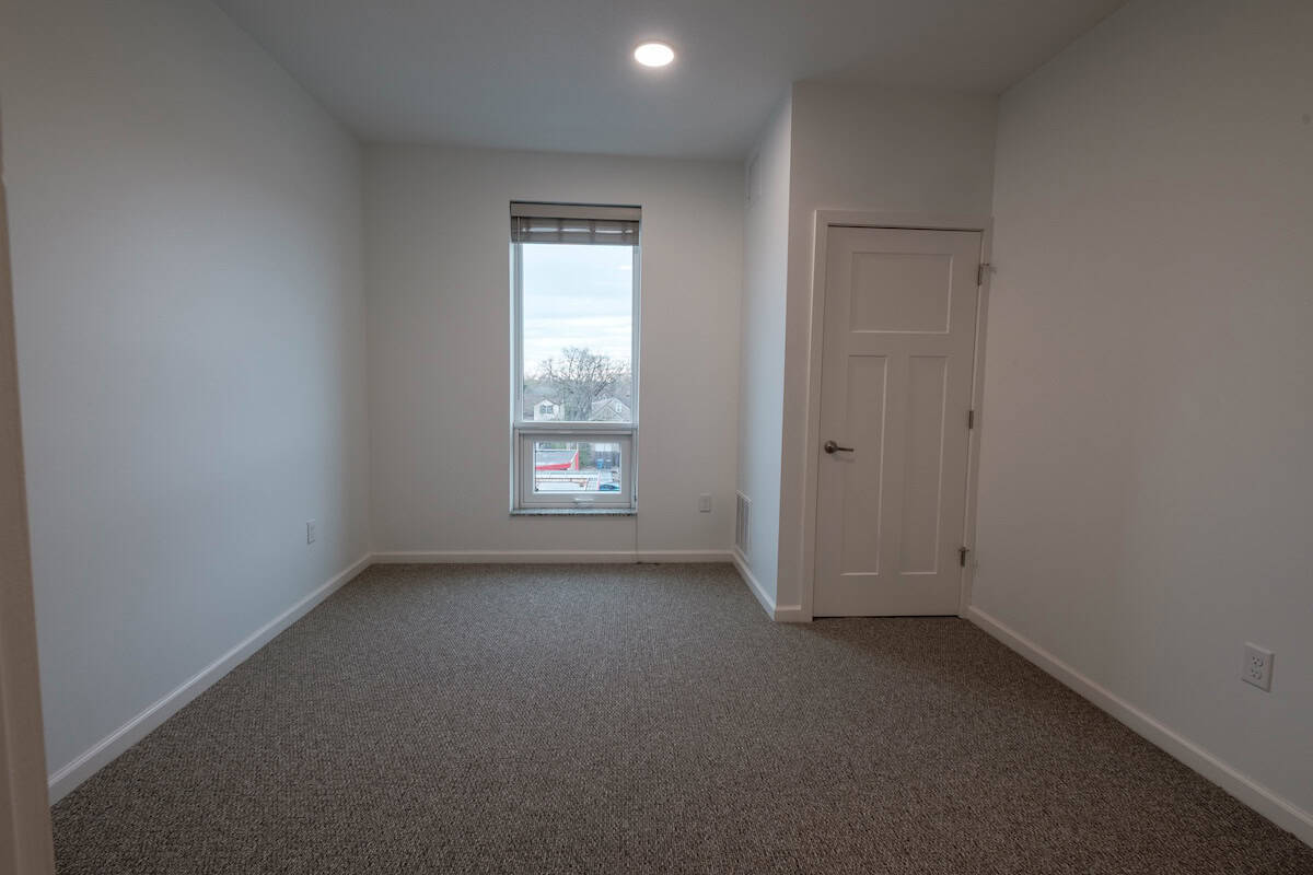 Bright, empty room with white walls, a single window, and a closed door.
