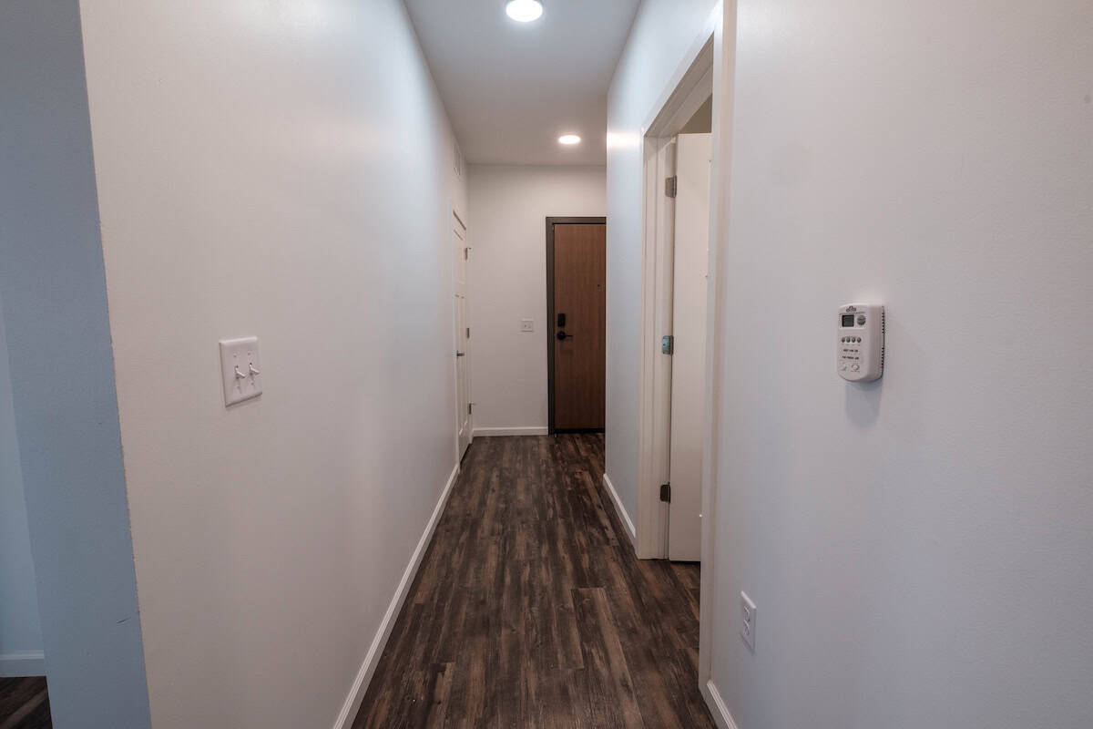 Modern apartment hallway with white walls and wood flooring.
