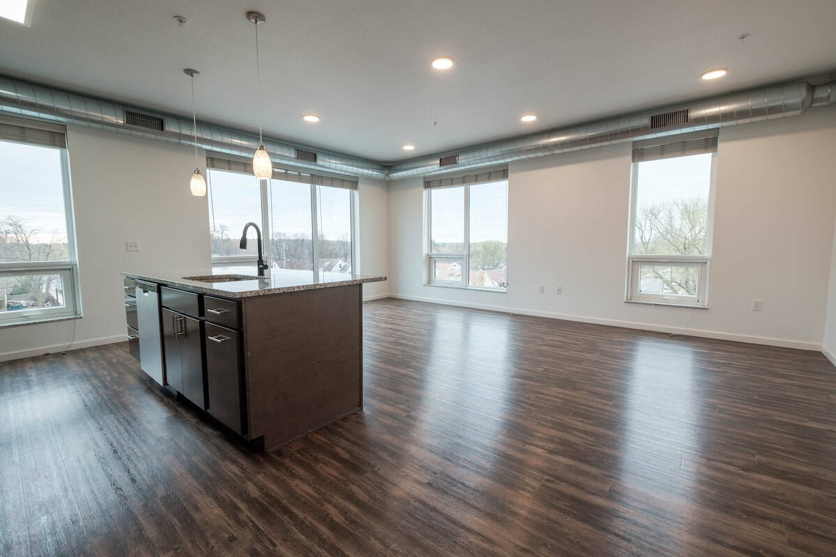 Modern apartment living room with large windows and hardwood floors.