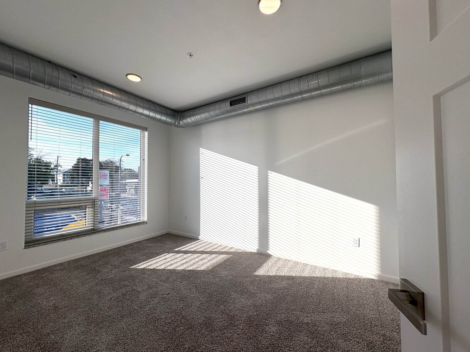Bright empty living room with natural sunlight and view of cityscape through windows.